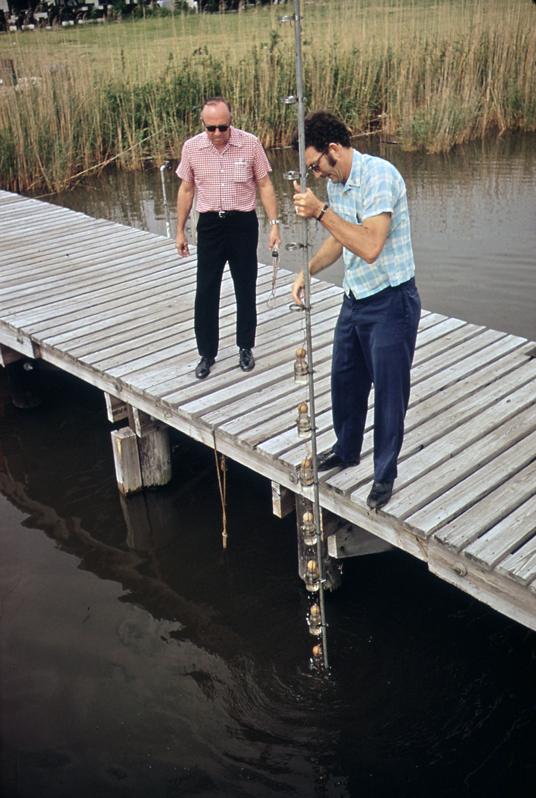 Two men on a dock on the river with measuring equipment